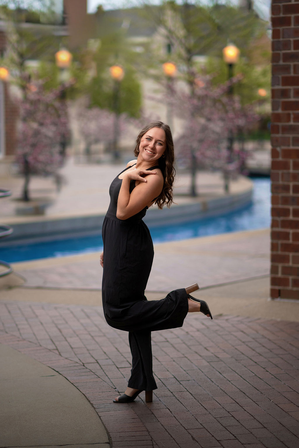 A happy high school grad in a black romper poses with a leg up behind her