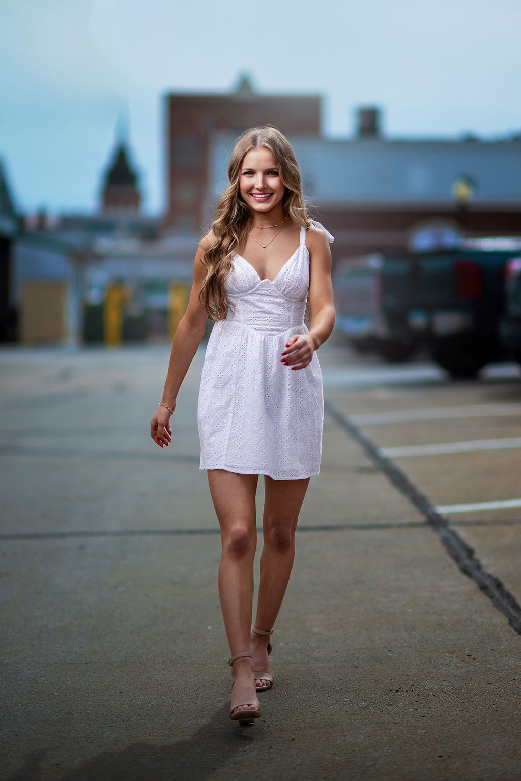 A high school senior in a white dress walks on the roof of a parking garage in downtown after visiting colleges near des moines