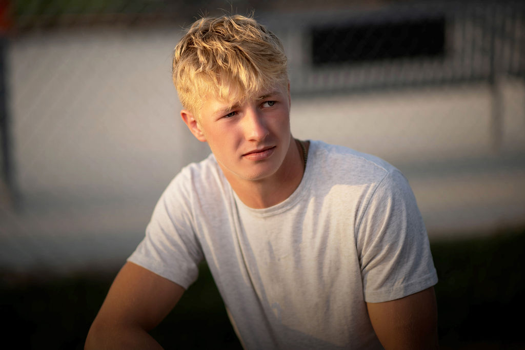 A high school senior in a grey shirt sits and leans on his knee in a grey shirt in the sun after attending dmacc career advantage