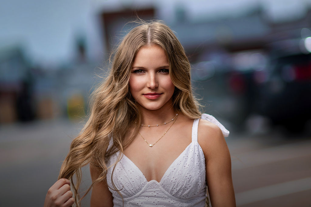 A blonde high school drag in a white top walks on the street playing with her hair after visiting hair salons in des moines