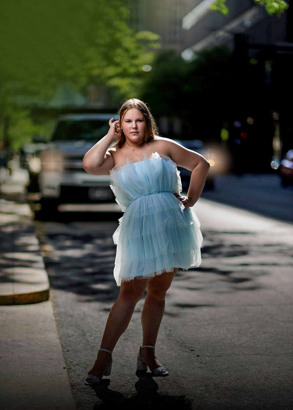 A high school senior stands in a downtown street with a hand in her hair and on her hip in a blue tule dress