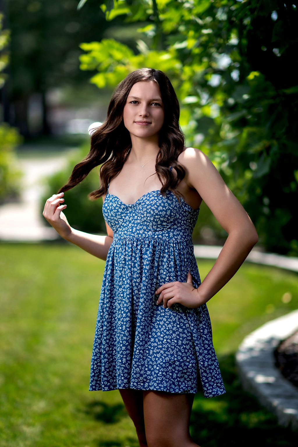 A high school senior twirls her brown hair while standing in a garden in a blue dress after shopping for homecoming dresses in des moines