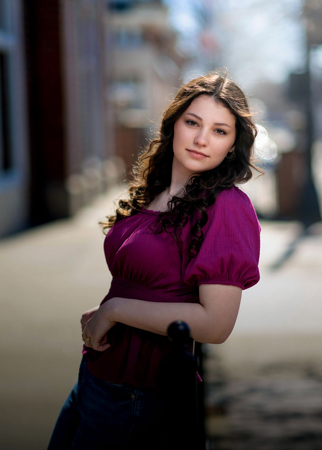 A woman in a purple blouse leans on a railing in the street smiling