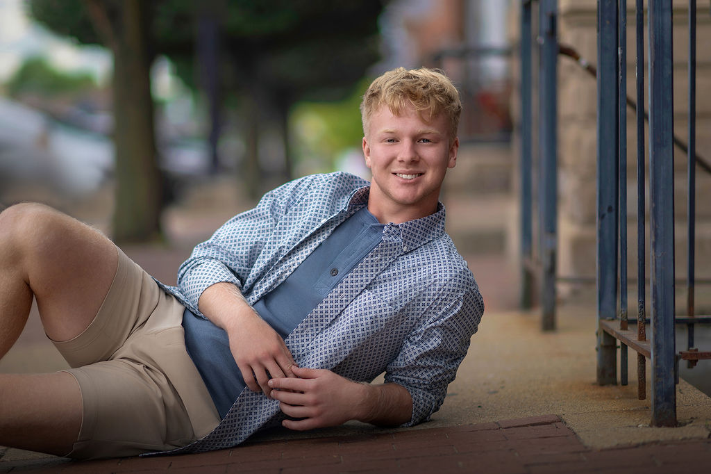 A man lays across the sidewalk in a blue shirt and khaki shorts for his iowa state graduation photos