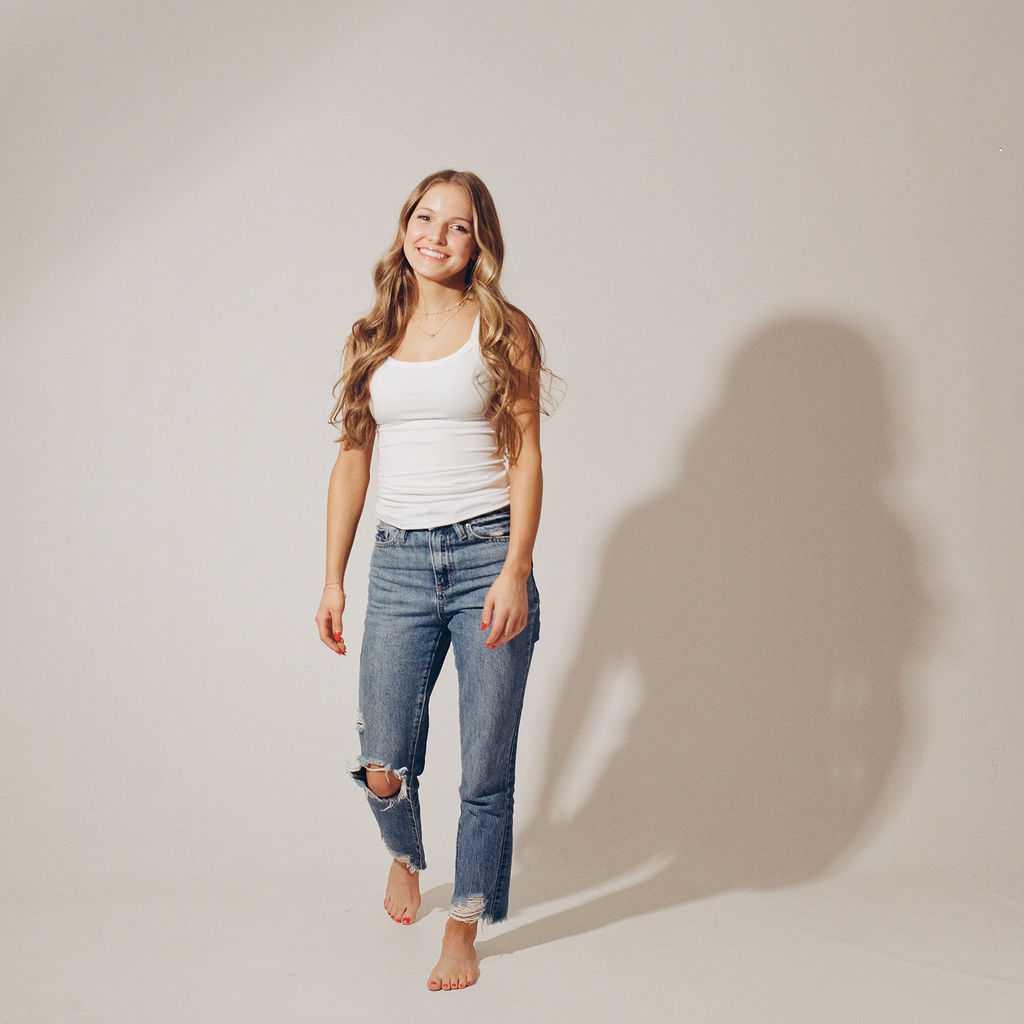 A high school grad walks in a studio in jeans and white top while smiling after visiting nail salons in des moines