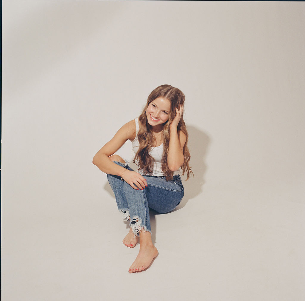 A high school senior sits in jeans and a whtie shirt with a hand in her hair after visiting nail salons in des moines