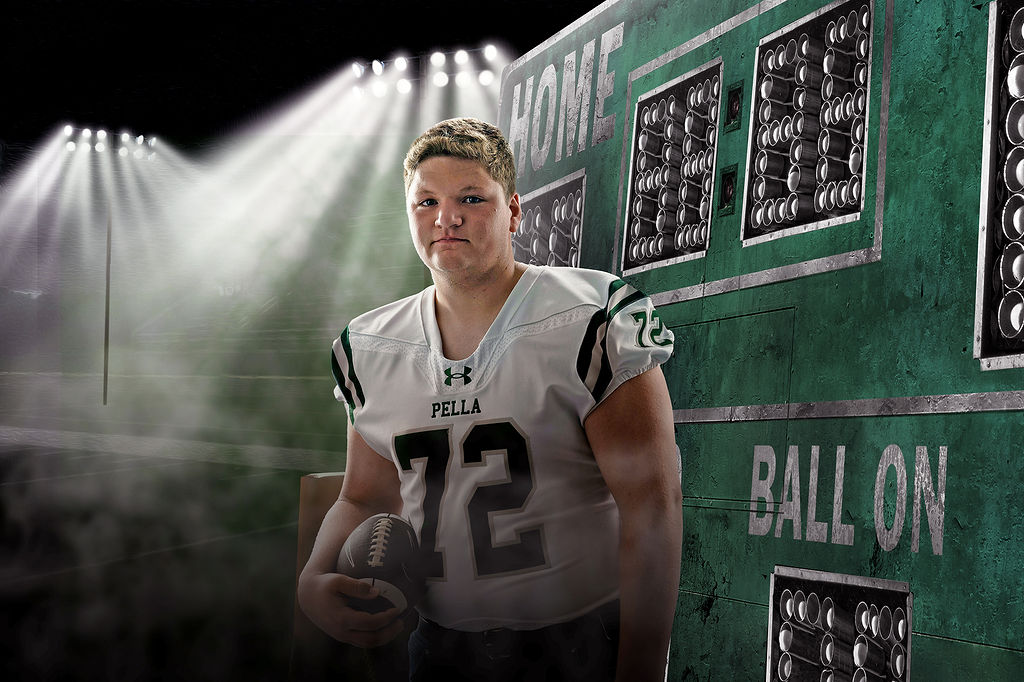 A football player stands in a football themed studio holding a ball in his jersey