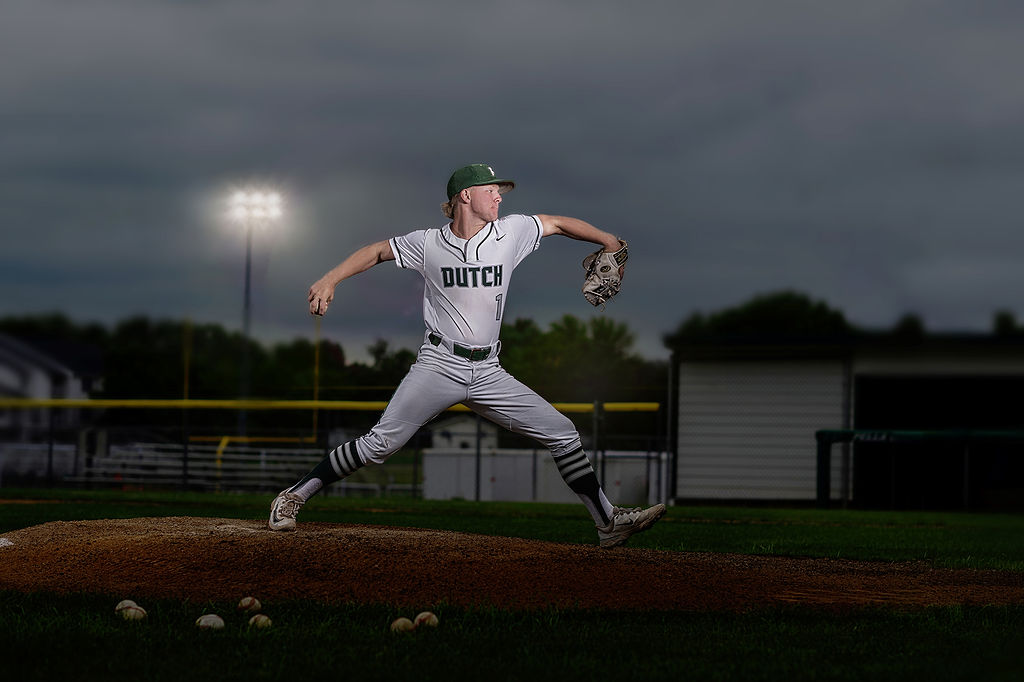 A baseball pitcher mid pitch on the mound in the evening in his pella high school jersey