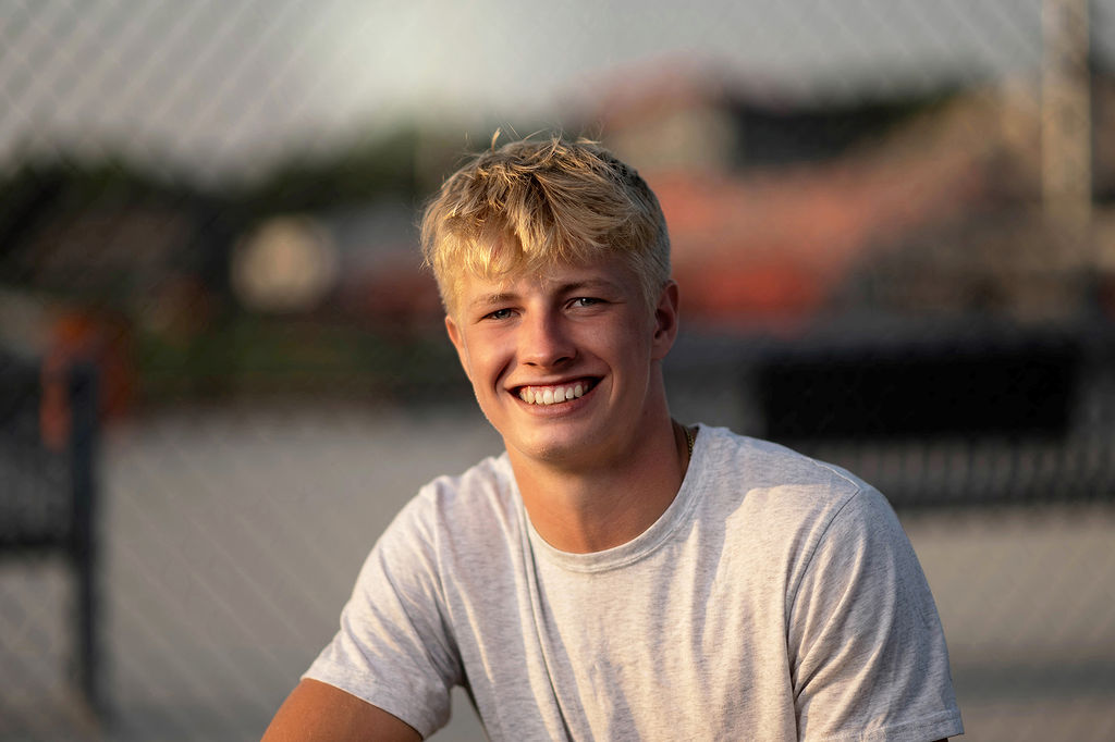 A blonde high school senior smiles while sitting in a grey shirt at sunset after attending private schools in Des Moines