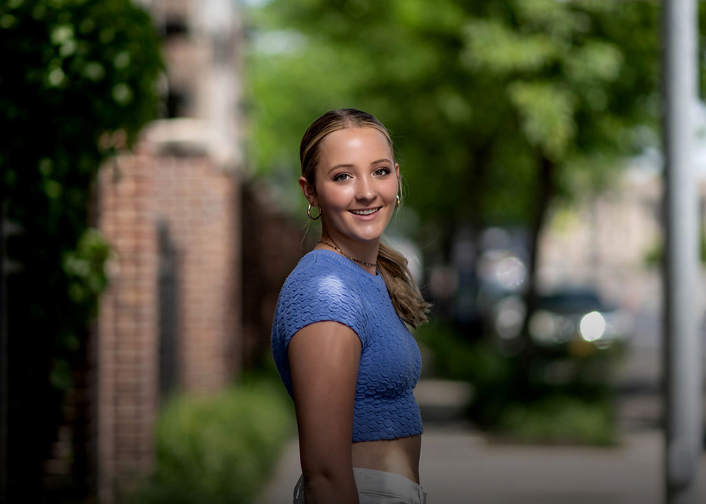 A roosevelt high school des moines senior walks on the street in a blue blouse while smiling over her shoulder