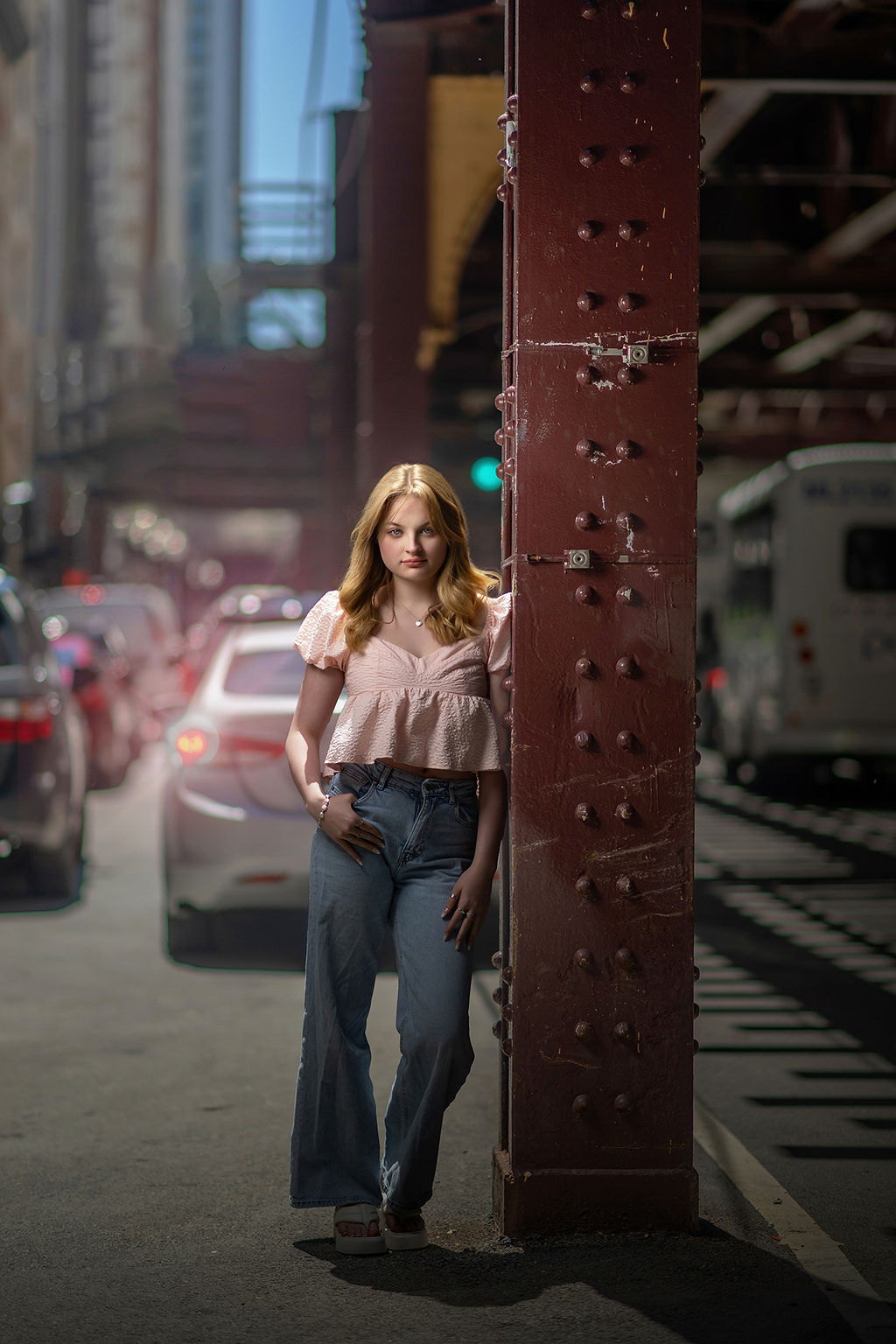 A high school senior leans against an iron beam on the street for her senior photos in des moines