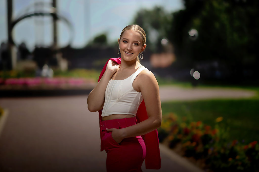 A happy high school graduate smiles over her shoulder while walking in a park in a white top and pink pants