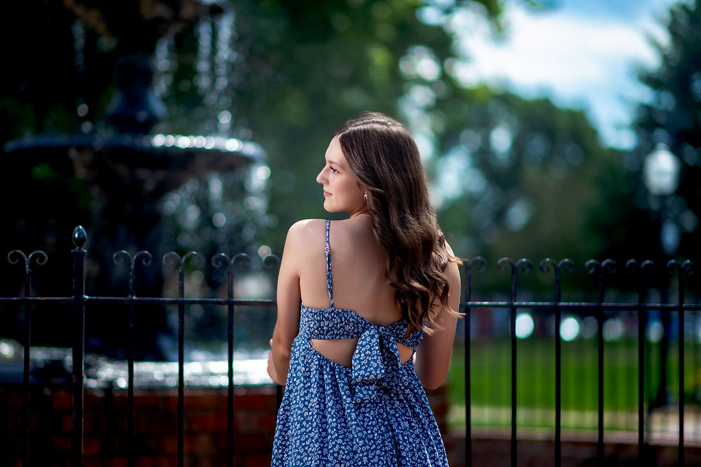 A woman in a blue floral dress leans on the iron fence of a fountain after visiting world food prize hall of laureates