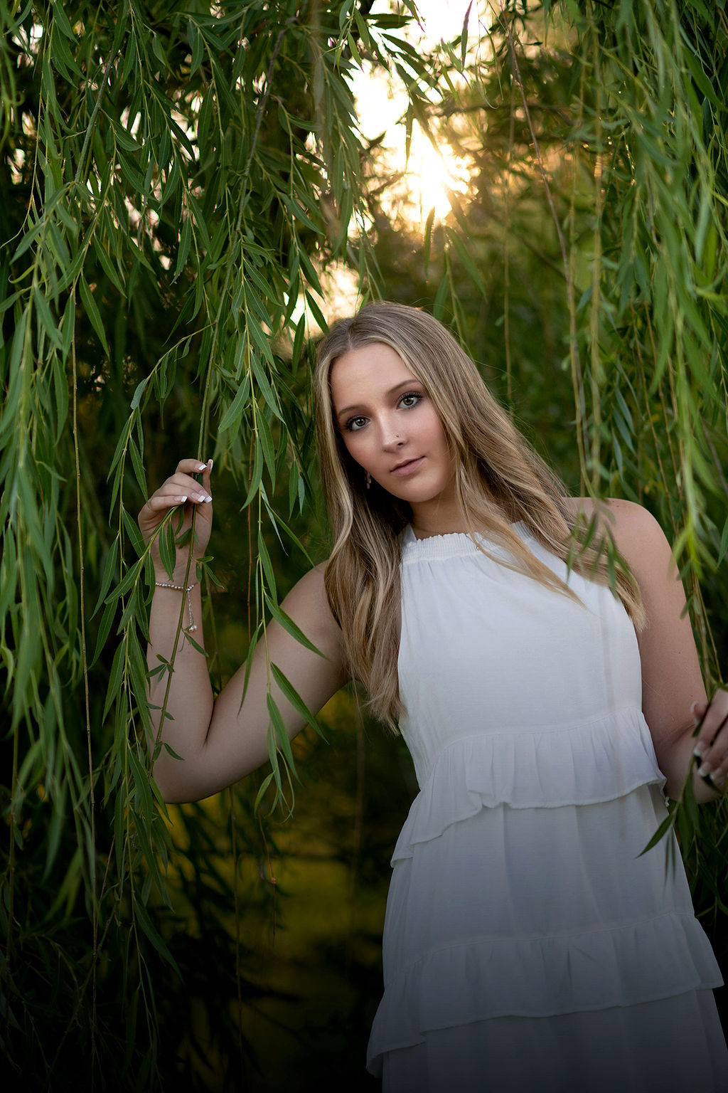 A high school senior in a white dress plays in the branches of a willow tree after visiting world food prize hall of laureates