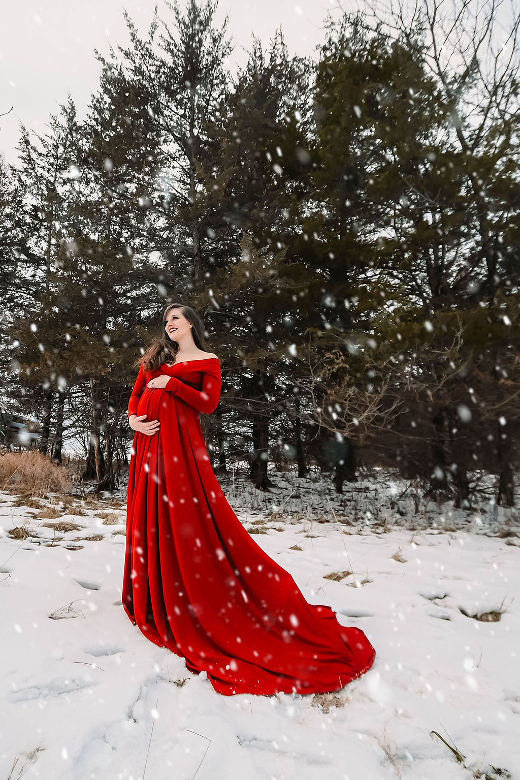 A smiling mother to be stands in a red maternity gown as snow falls around her after her 3d ultrasound in des moines