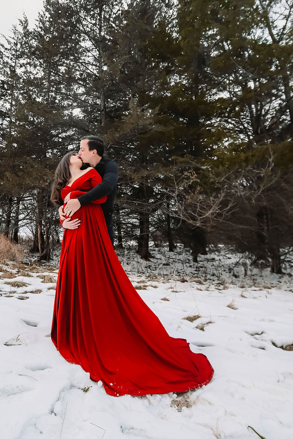 A happy pregnant couple kisses in a snowy forest with hands on the bump after a 3d ultrasound in des moines