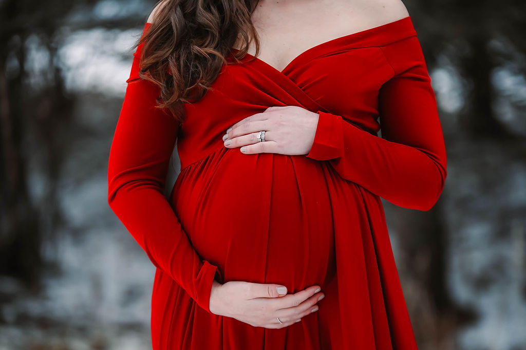 Details of a expecting woman's bump in a red maternity gown with hands on top and bottom