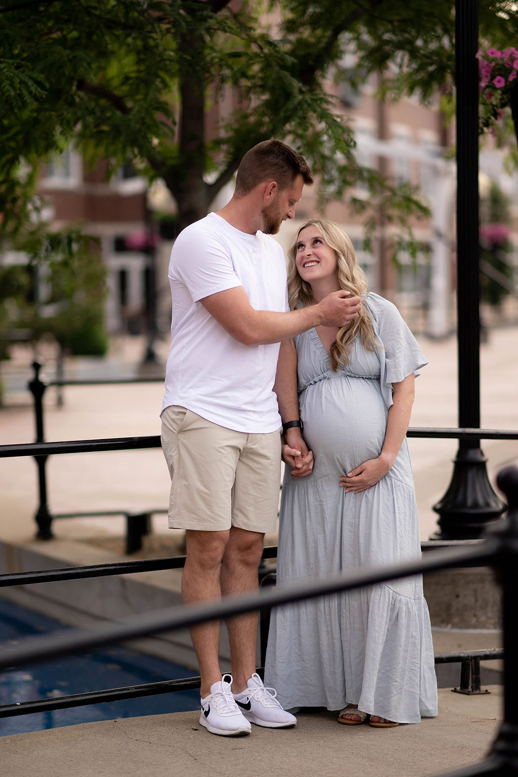 A man stands with his pregnant wife on a bridge pulling her hair back as she smiles up to him after finding Blessings in Birth