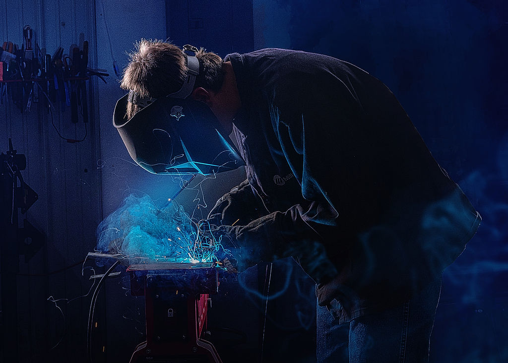 A high school grad welds under blue light in a shop