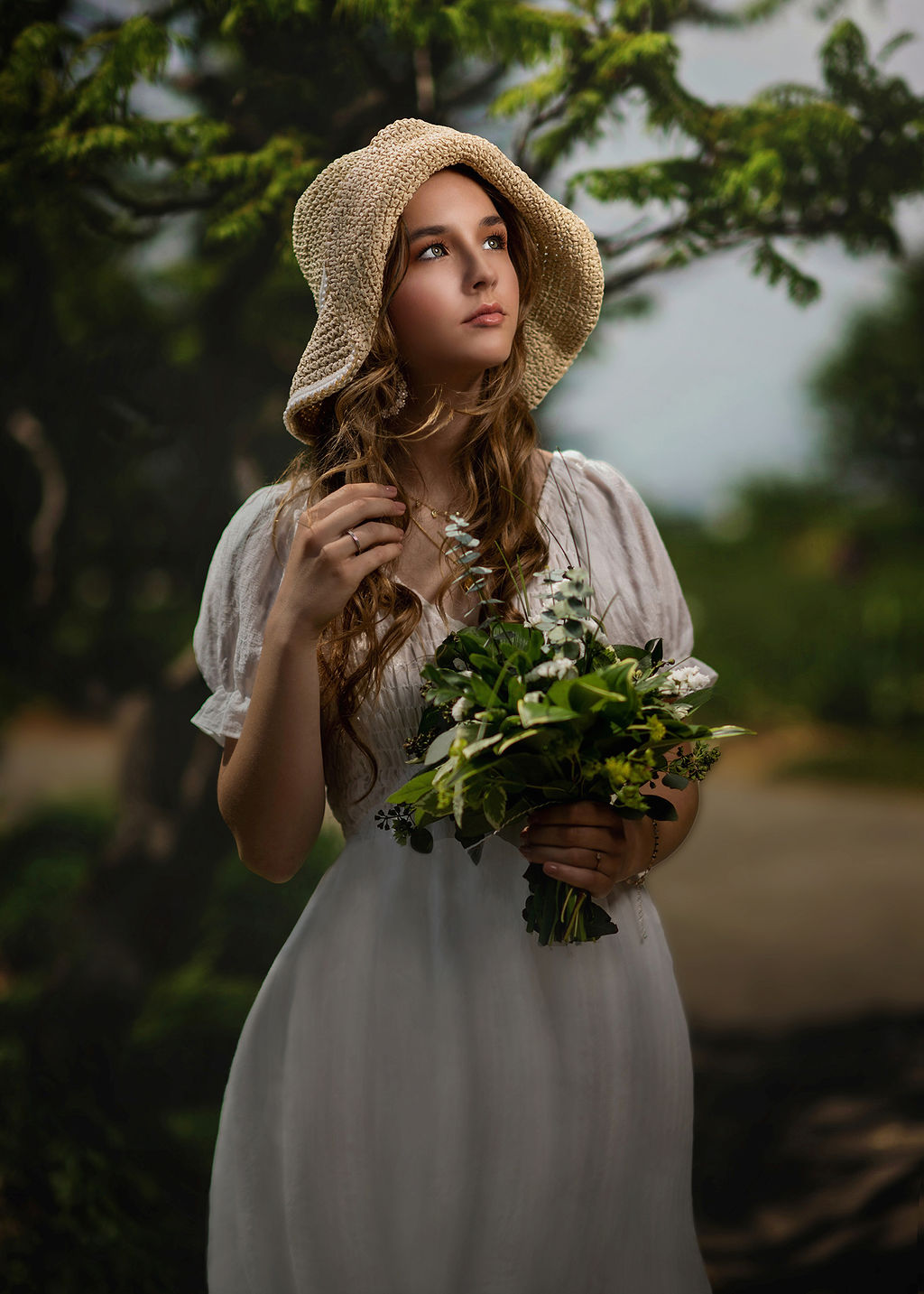 An Oskaloosa High School senior in a white dress and brown floppy hat holds a green bouquet