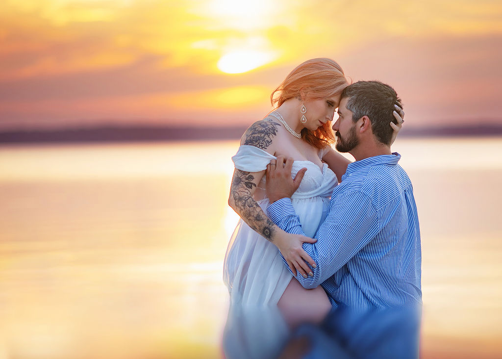 A pregnant couple shares and intimate moment in the water at sunset after visiting baby shower venues in Des Moines