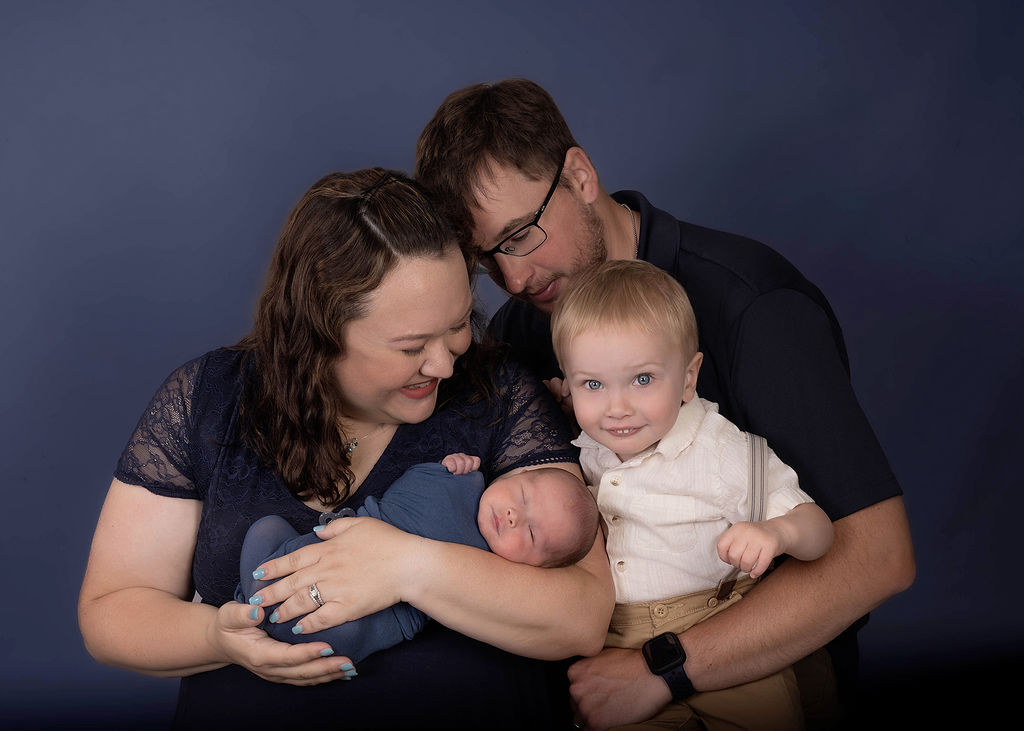 A happy family cuddles in a studio with a newborn baby and toddler son