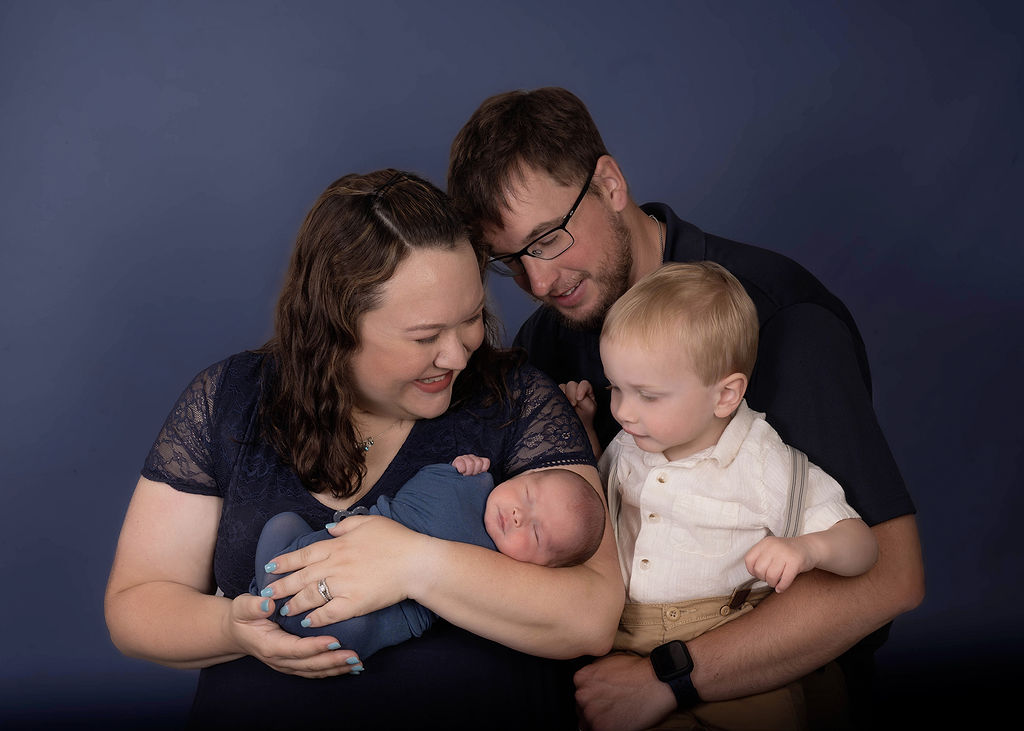 Happy parents smile while showing their newborn baby to their toddler son in a studio after visiting Daycares in Des Moines