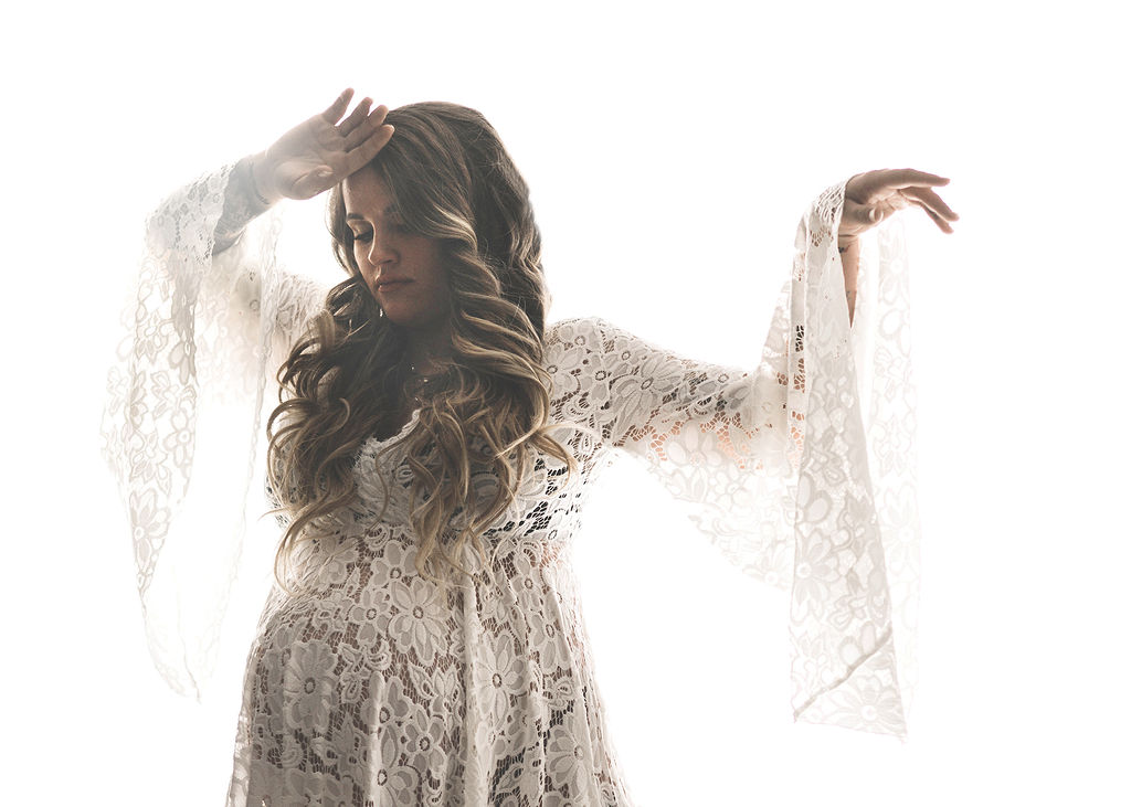 A mom to be dances in a lace dress in a studio with her hands up after meeting des moines midwives