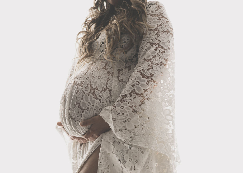 Details of a mother to be's bump in a lace dress in a studio