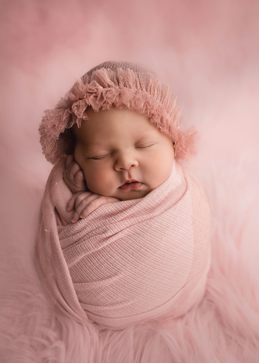 A newborn baby girl sleeps in a pink swaddle and cap in a studio after meeting iowa baby lady