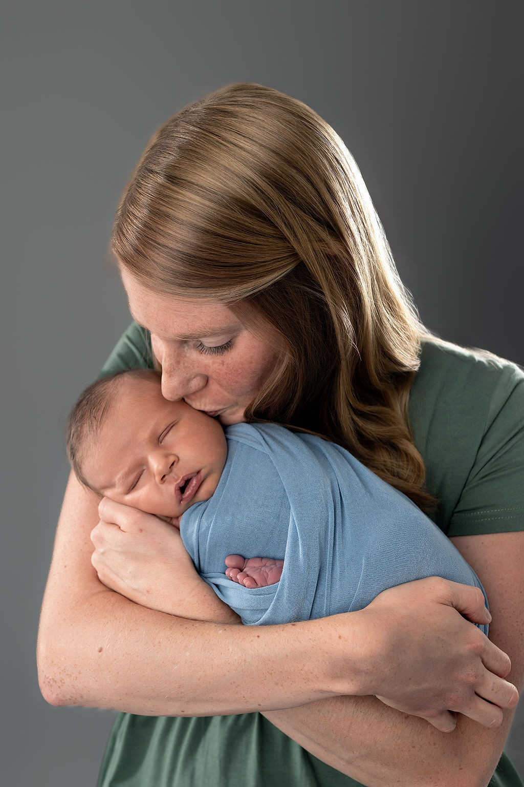 A new mom in a green dress kisses her newborn baby son in her arms in a studio after meeting a lactation consultant in Des Moines