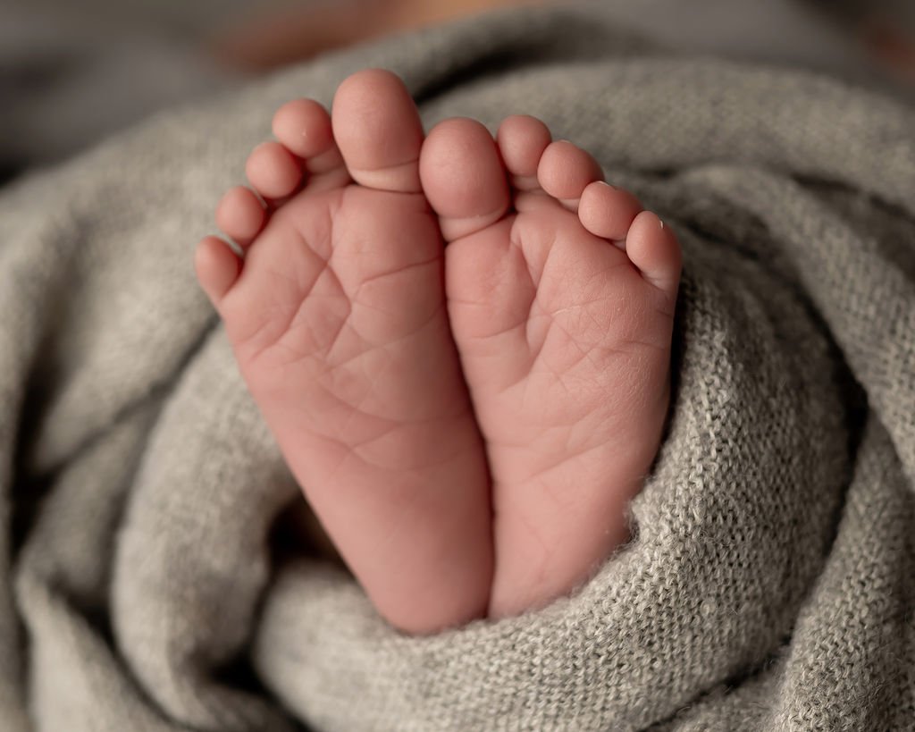 Details of a newborn baby's feet wrapped in a grey blanket