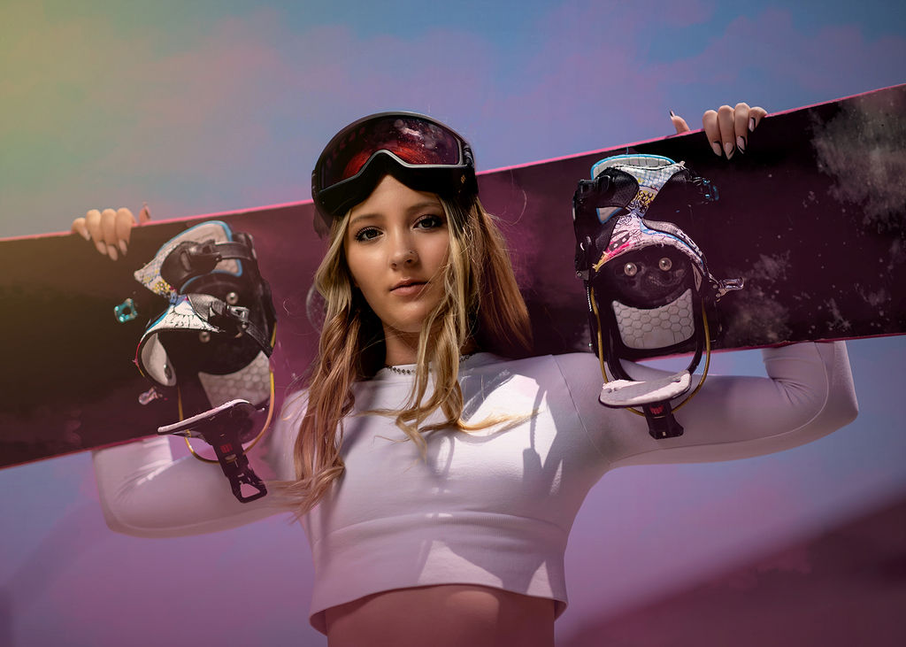 A high school senior in a white top holds a snowboard behind her head after visiting nail salon in pella, iowa