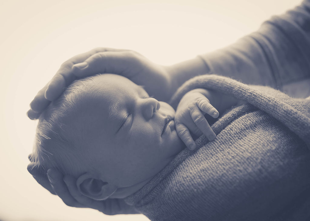 Details of a sleeping newborn baby with dad's hands on his head after some parenting classes in des moines