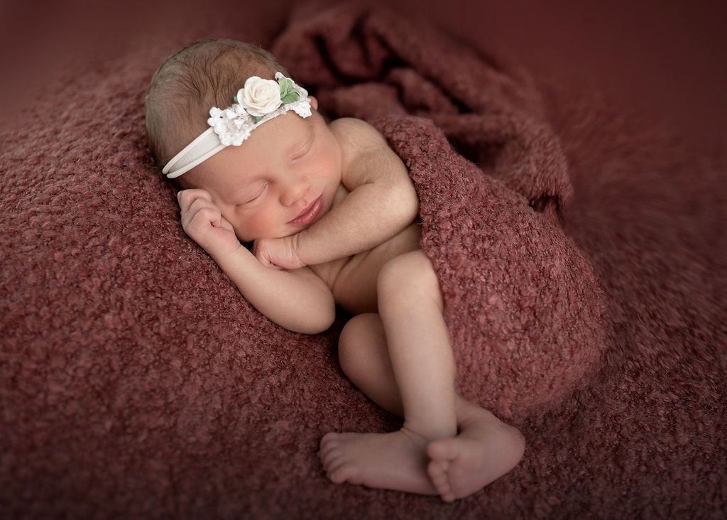 A happy newborn baby sleeps with a smile in a red blanket in a studio after visiting a pediatric dentist in des moines