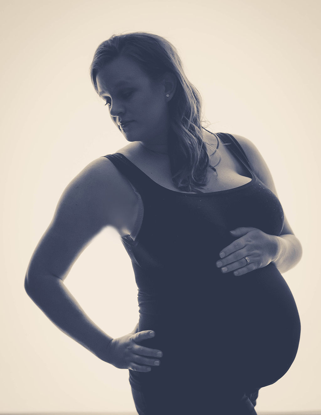 A mom to be in a black maternity gown looks over her shoulder in black and white after visiting a pella obgyn