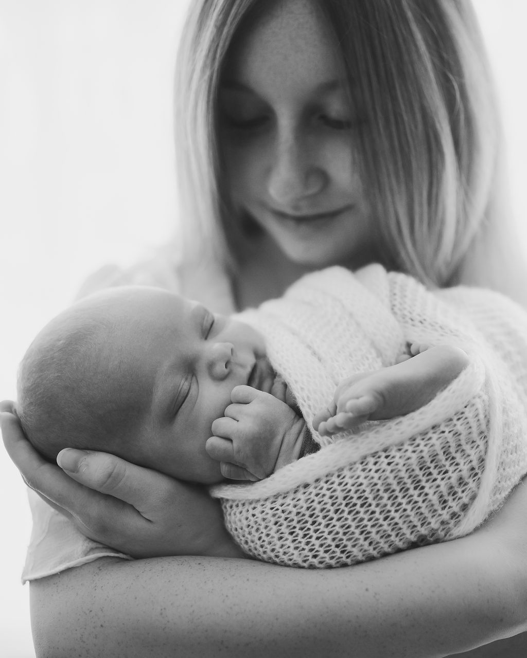 A newborn baby sleeps in a knit swaddle in mom's arms in a studio in black and white before some pelvic floor therapy in Des Moines