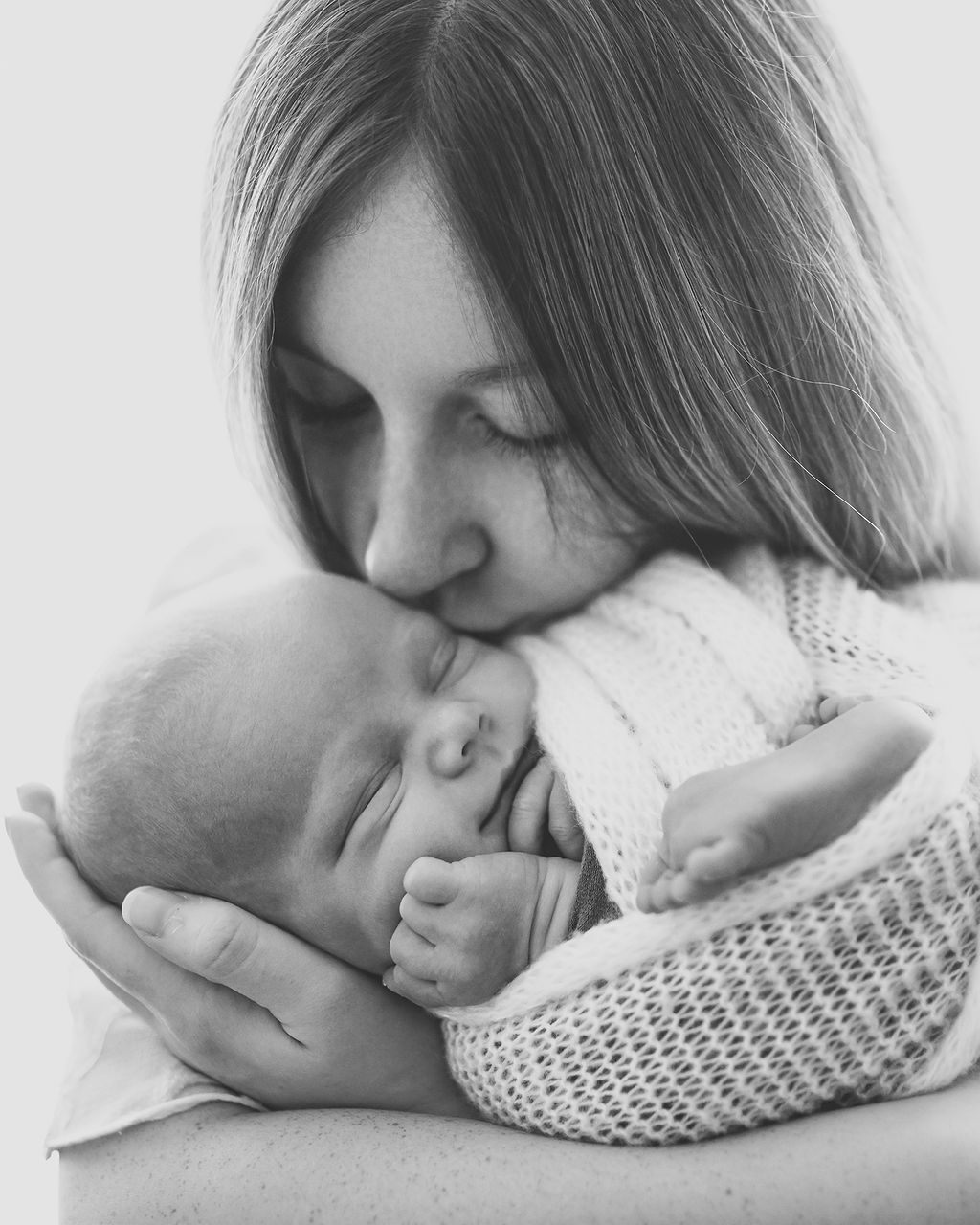 A newborn baby smiles while swaddled in mom's arms as she kisses the baby before some pelvic floor therapy in Des Moines