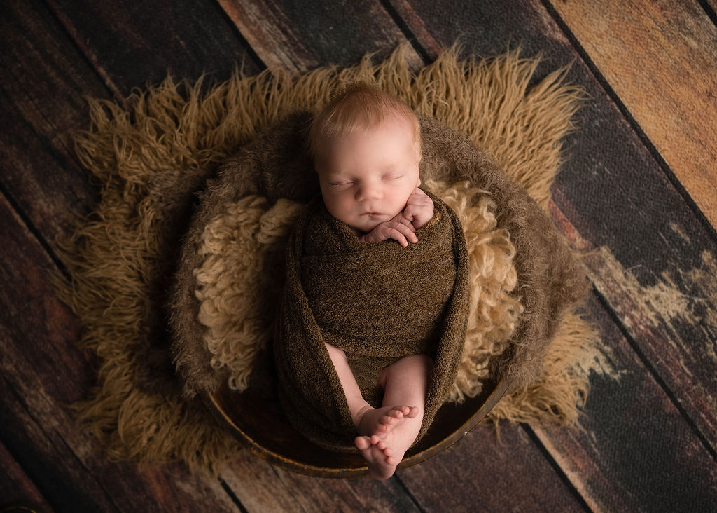 A newborn baby sleeps in a wooden bowl in a matching knit swaddle with feet out after mom found placenta encapsulation in des moines