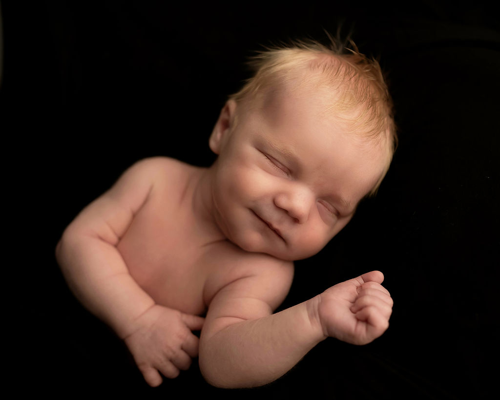 A newborn baby smiles in its sleep in a studio after mom got placenta encapsulation in des moines