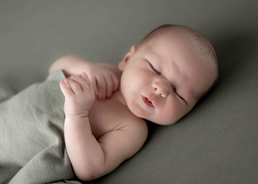 A newborn baby makes a silly face under a green blanket after using Baby Butler