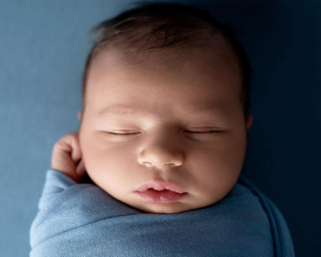 Closeup of a sleeping newborn baby in a blue swaddle after visiting Basking Babies