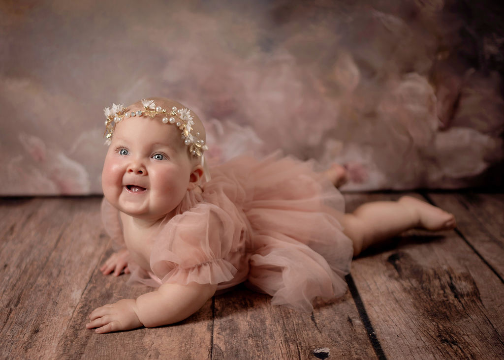 A baby crawls on hardwood floor in a studio in a pink tule dress and pearl headband before visiting a Daycare in Pella, Iowa