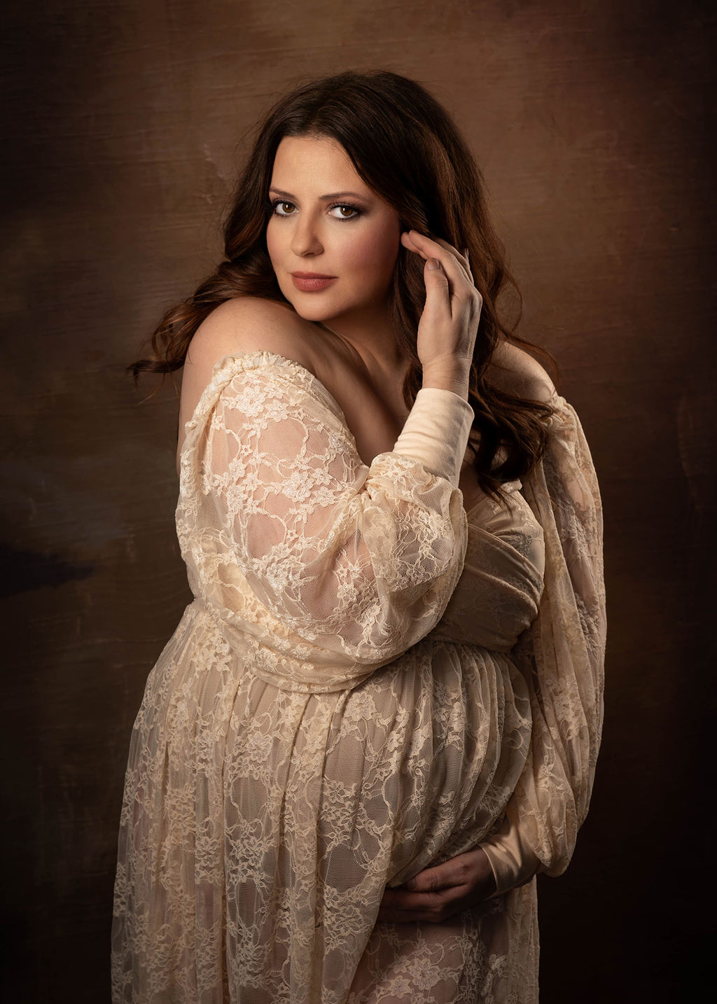 A mother to be in a yellow lace maternity gown stands in a sstudio pulling her hair back after meeting des moines midwife collective