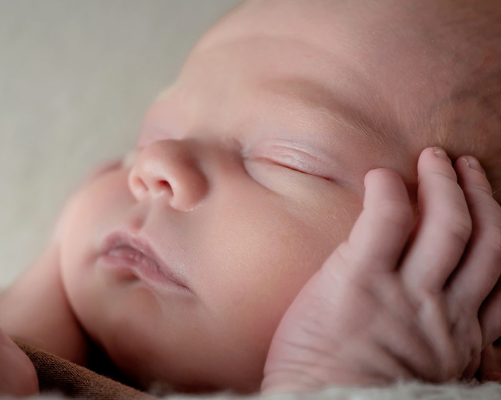 Details of a newborn baby with hands on its cheek