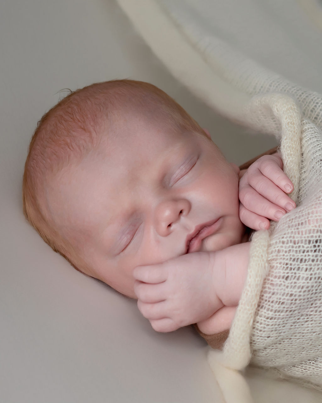 A newborn baby sleeps under a cheesecloth swaddle in a studio after using Heart Of Iowa Midwifery