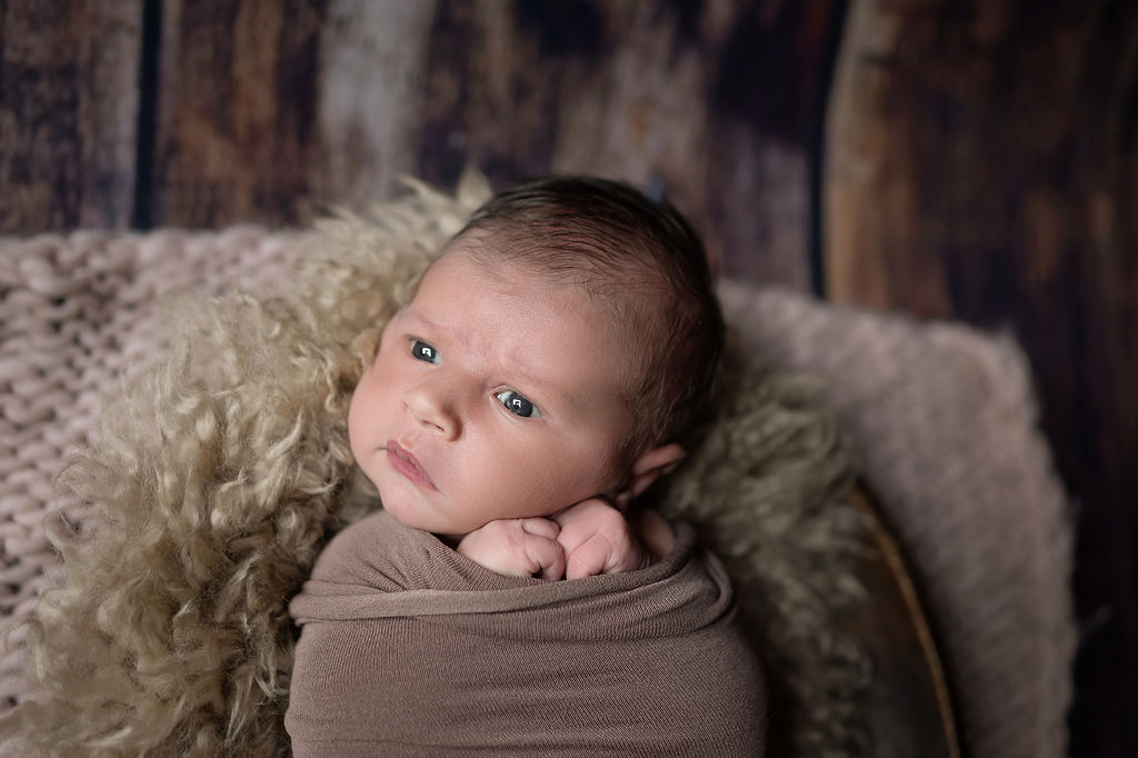 A cloesup image of a newborn baby with eyes open in a studio