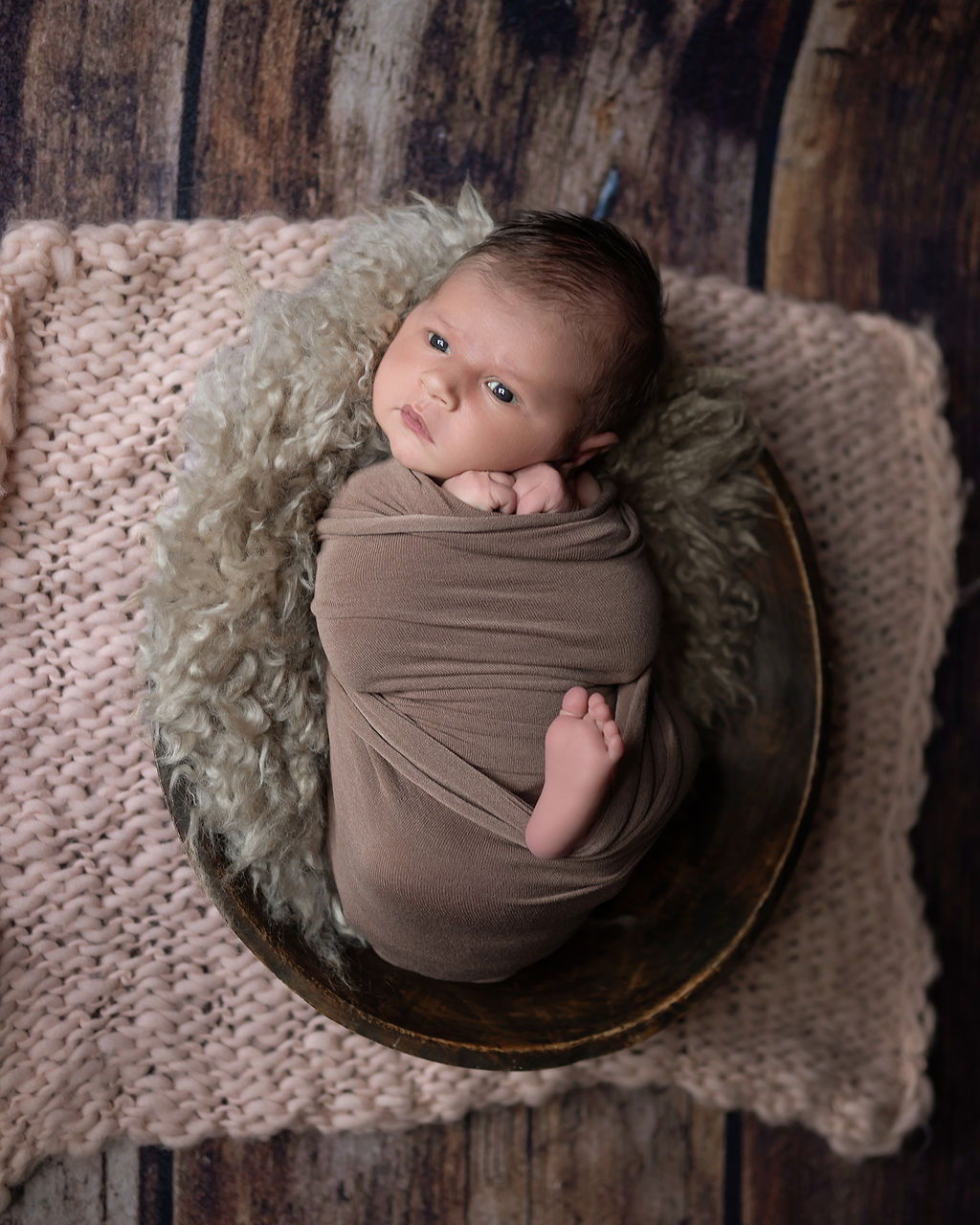 A curious newborn lays in a wooden bowl on hardwood floor in a studio with eyes open after visiting Ivory Soul