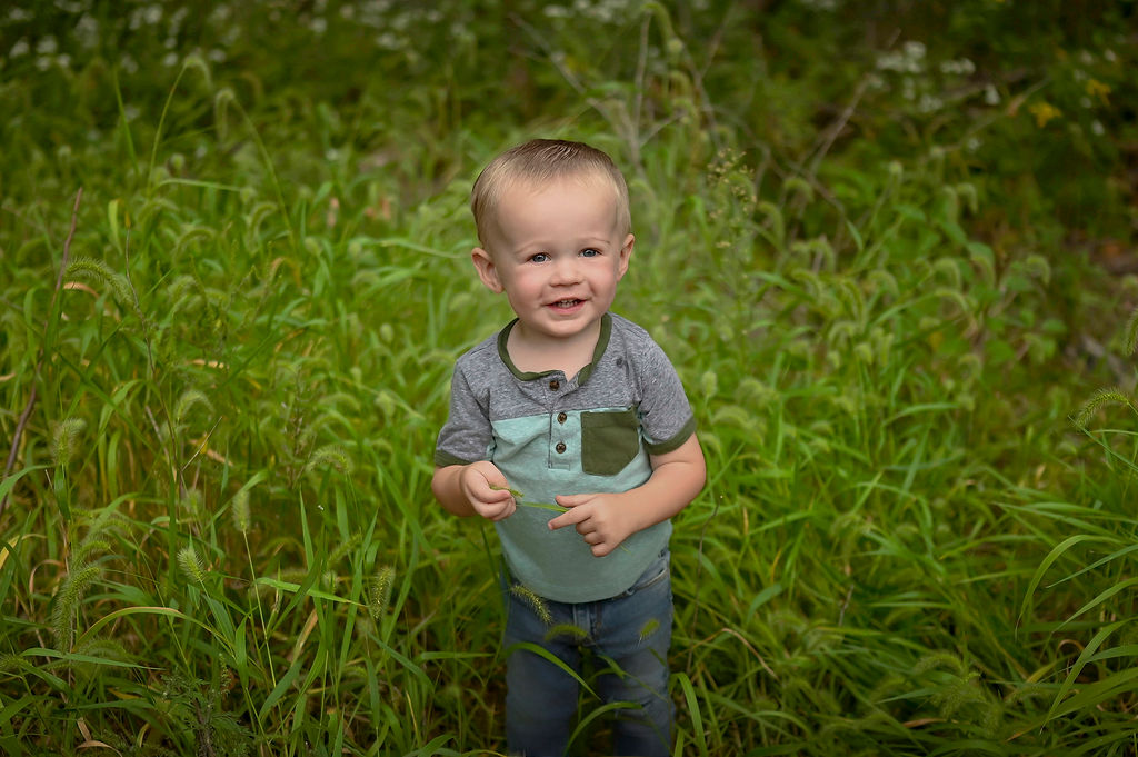 A baby boy in jeans explores tall grass in a park