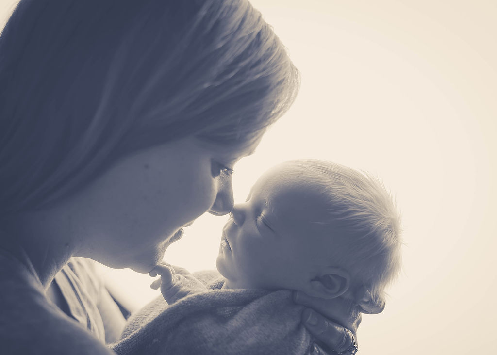 A mom touches noses with her sleeping newborn baby in black and white